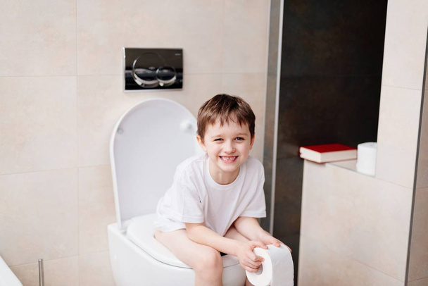 Little 7 years old boy sitting on toilet. - Photo, Image