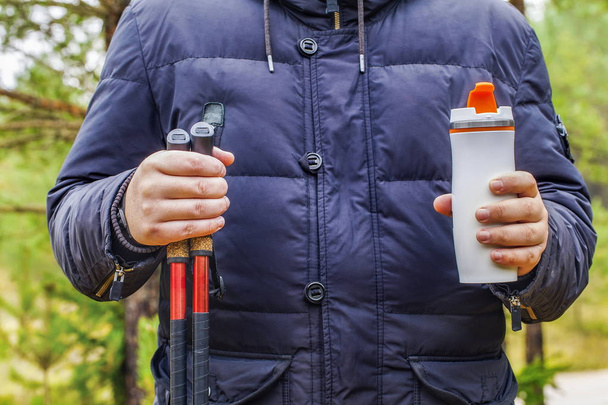 Wanderer hält Pokal mit Getränken und Wanderstöcken in der Hand - Foto, Bild