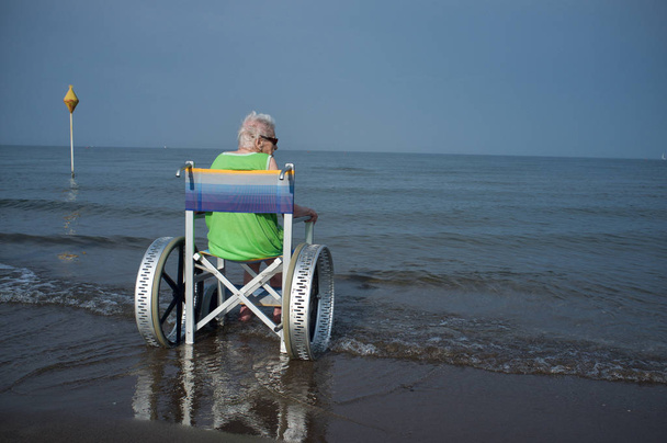 ηλικιωμένη γυναίκα σε μια αναπηρική καρέκλα στη θάλασσα - Φωτογραφία, εικόνα