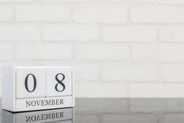 Gros plan calendrier en bois blanc avec mot noir 8 novembre sur table en verre noir et fond texturé mur de briques blanches avec espace de copie, mise au point sélective au calendrier
 - Photo, image