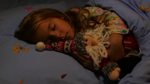 Χαριτωμένο κορίτσι κοιμάται στο κρεβάτι αγκαλιάζει Αϊ-Βασίλη παιχνίδι. Κοντινό πλάνο - Πλάνα, βίντεο