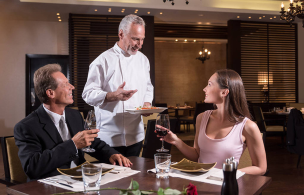 Smiling positive chef representing his dish to the couple - Foto, Imagem