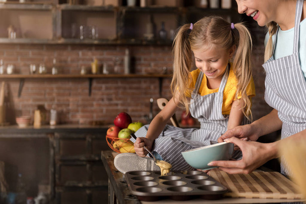 Smiling involved girl helping her mother cooking pastry - Фото, зображення