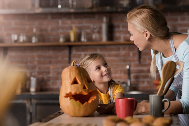 Smiling girl preparing a pumpkin for Halloween with her mother - Foto, imagen