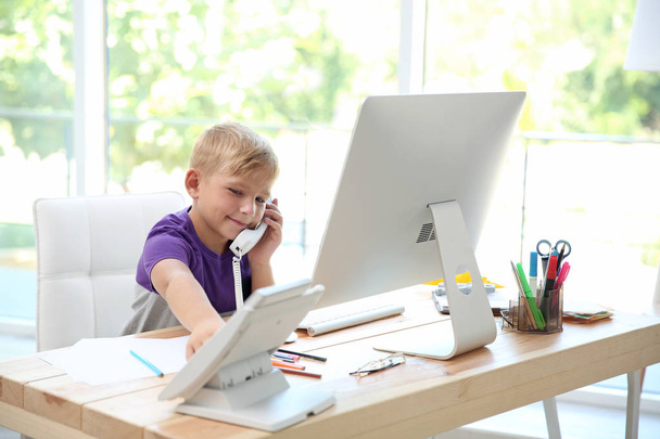 Little boy talking on phone at father's table in office - Photo, image