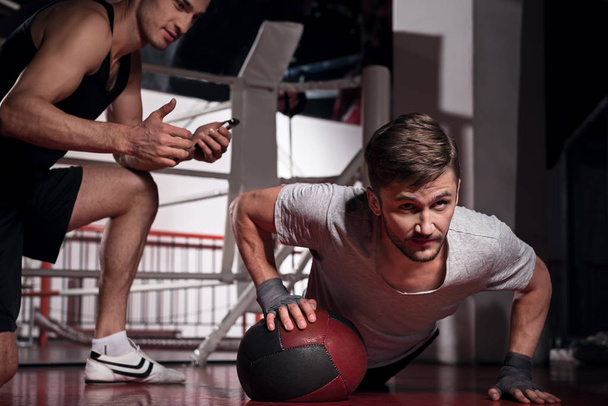 Man doing push-ups with trainer using fitness ball - Фото, зображення