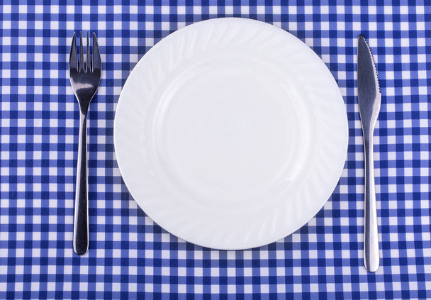 leerer Teller und mit einer Messergabel auf der Tischdecke im Käfig - Foto, Bild
