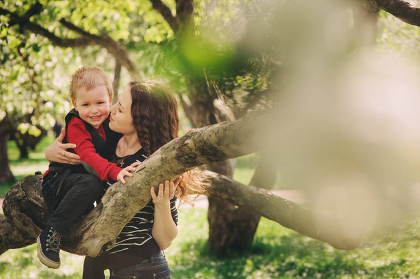 happy mother and toddler son playing together outdoor and climbing apple tree in spring or summer - Foto, Imagen