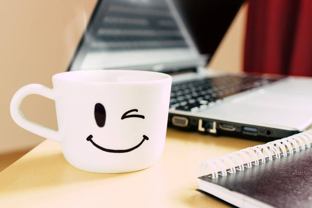 Smiling cup, notepad and laptop on the desk - Foto, imagen