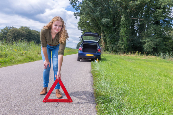 Mujer holandesa colocando triángulo de advertencia en camino rural
 - Foto, imagen