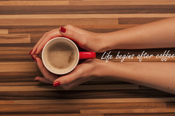 LIFE BEGINS AFTER COFFEE, Female hands holding a cup of coffee with foam over wooden table, top view. - Zdjęcie, obraz