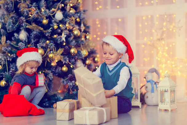 Crianças abrindo presentes de Natal na sala de estar decorada
 - Foto, Imagem