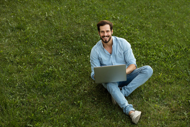 Young man in casual jeans outfit lying down with his laptop in f - Foto, afbeelding