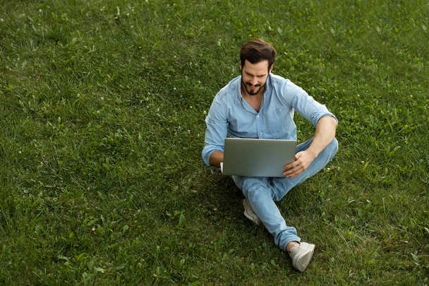 Young man in casual jeans outfit lying down with his laptop in f - Zdjęcie, obraz