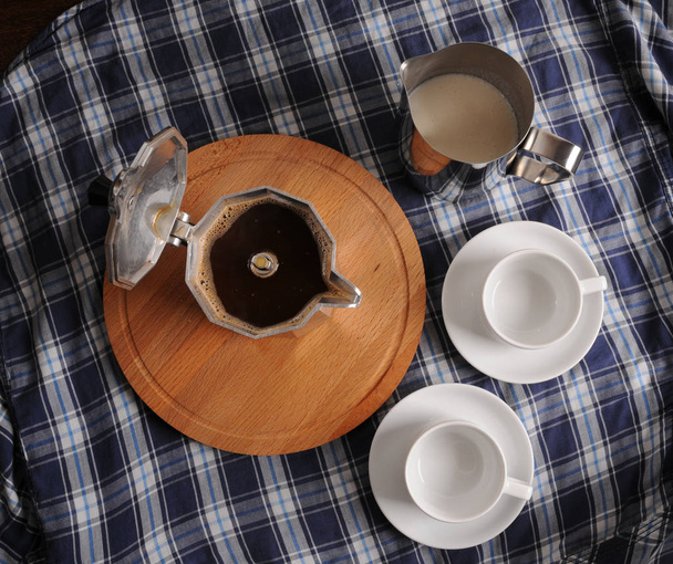 Кава Гейзера на круглому обробному дошці, глечик молока та чашок на синій скатертині
 - Фото, зображення