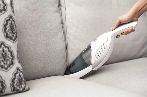 Woman with handheld vacuum cleaning on sofa - Valokuva, kuva