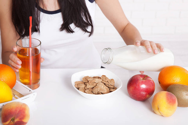 Woman sits at a table and eat breakfast. Women eating healthy food for breakfast. Fruit, cereal and milk, close up selective focus. - Foto, afbeelding