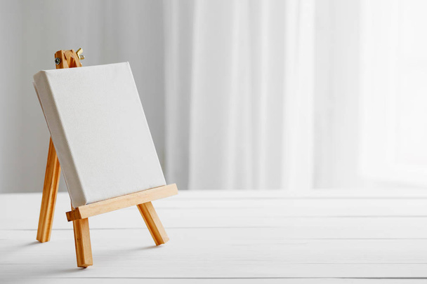 Empty canvas on easel on white wooden desk. - Фото, изображение
