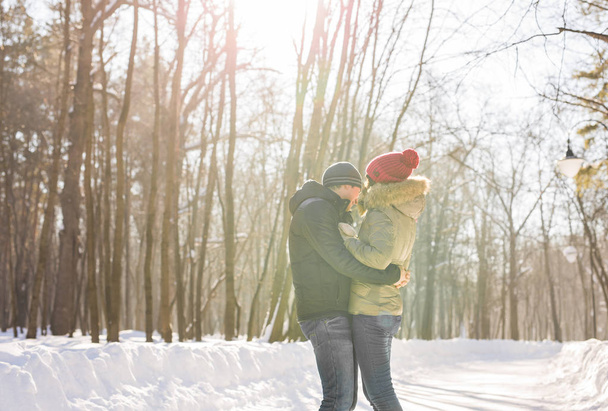 Νεαρό ζευγάρι αγκάλιασμα και το φίλημα στο πάρκο το χειμώνα. - Φωτογραφία, εικόνα