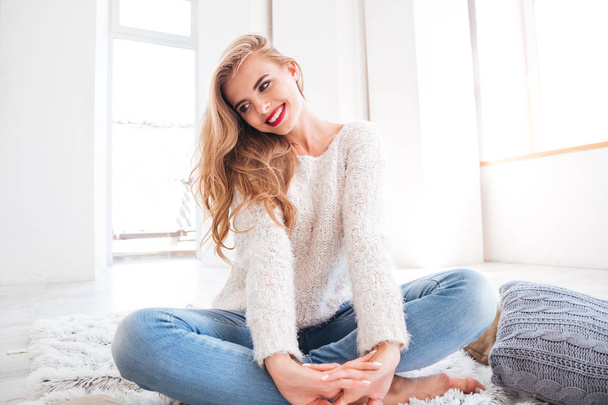Beautiful young woman in sweater sitting on the carpet - Фото, зображення