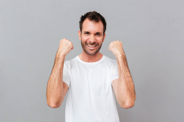 Happy excited young casual man celebrating success over grey background - 写真・画像