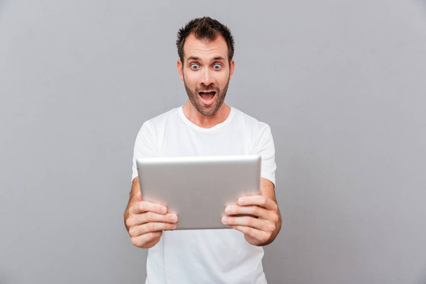 Surprised young man holding tablet over grey background - Foto, Imagen