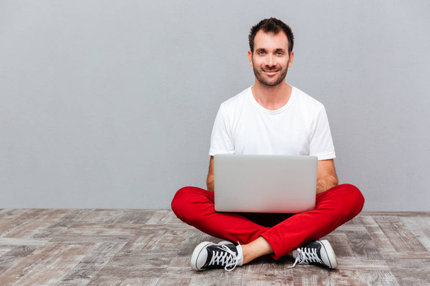 Happy casual man sitting on the floor with laptop - Zdjęcie, obraz
