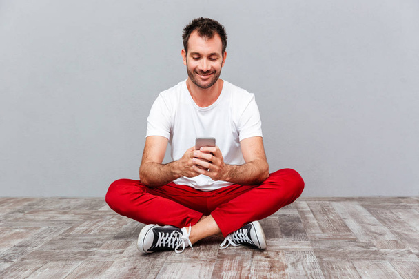 Happy casual man sitting on the floor and using smarpthone - Foto, imagen
