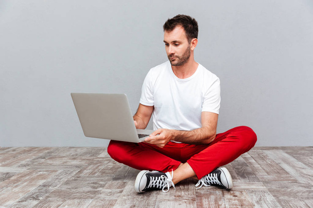 Pensive casual man sitting on the floor with laptop - Fotó, kép