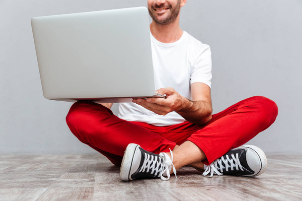 Happy smiling casual man sitting on the floor with laptop - Fotó, kép