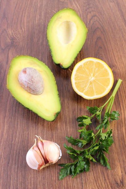 Avocado, garlic, lemon and parsley on wooden background, ingredient of avocado paste or guacamole, healthy food and nutrition - Photo, image