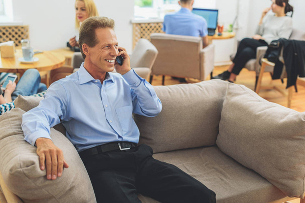 Joyful man communicating on telephone at work - Фото, изображение