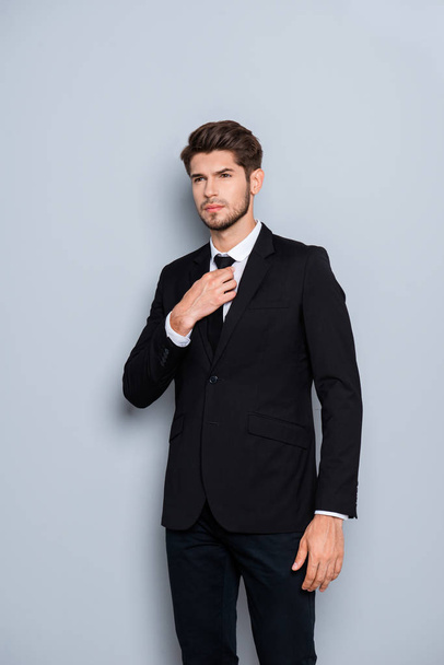 Portrait of stylish man in black suit correcting tie - Foto, Imagen