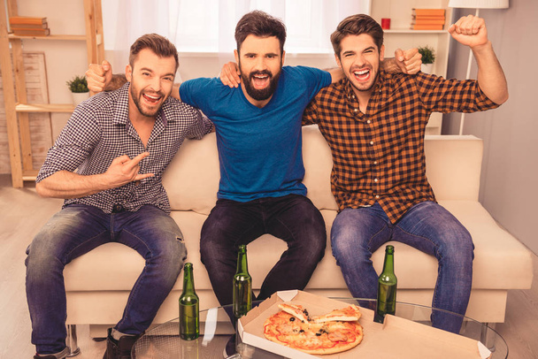 Portrait of three happy  men holding bottle of beer and watching - Foto, afbeelding