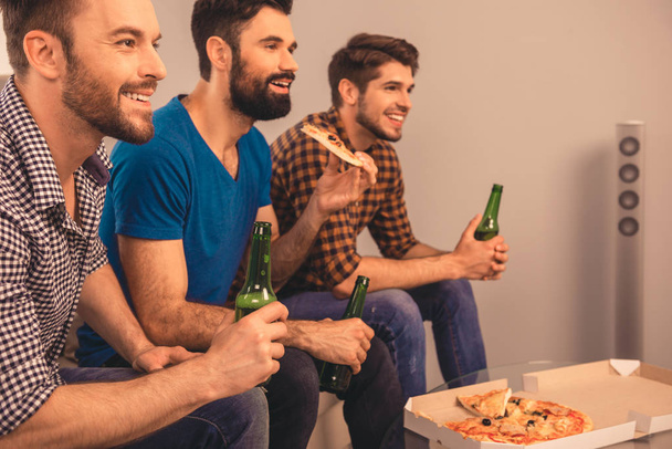 Side view of three men watching sport tv with beer and pizza - Zdjęcie, obraz
