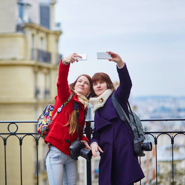Two cheerful girls in Paris taking selfie using mobile phone on Montmartre - Fotó, kép