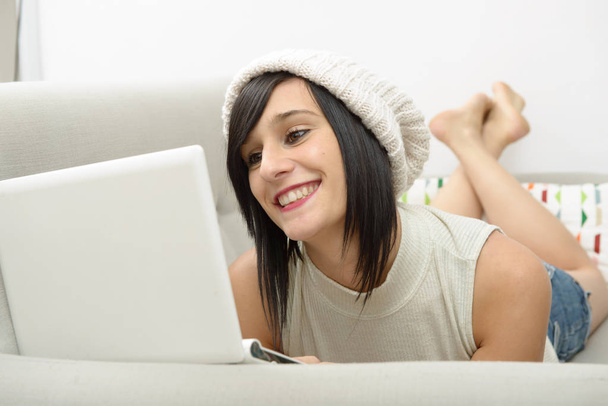 young brunette student lying on the couch with a laptop - Photo, Image