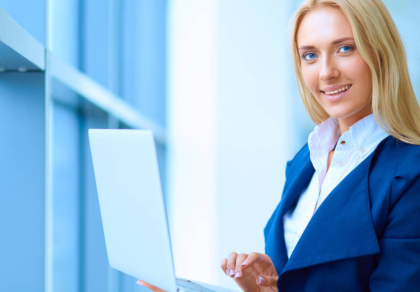 Businesswoman standing against office window holding laptop - Foto, Imagen