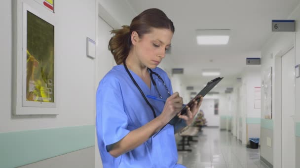 Nurse takes notes on clipboard outside room - Imágenes, Vídeo