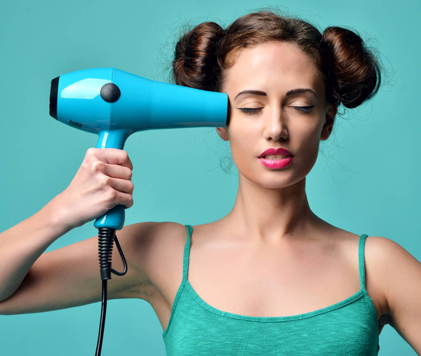 Happy young curly brunette woman with hair dryer on blue mint ba - Фото, изображение