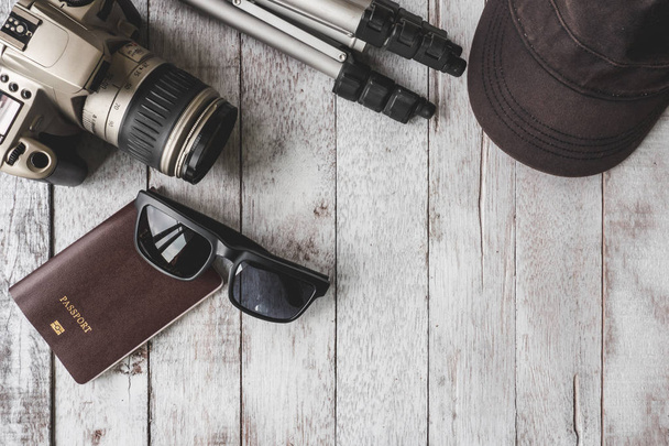 Top view of Camera with tripod,cap,sunglasses and passport on white wooden table background, Travel concept - Φωτογραφία, εικόνα