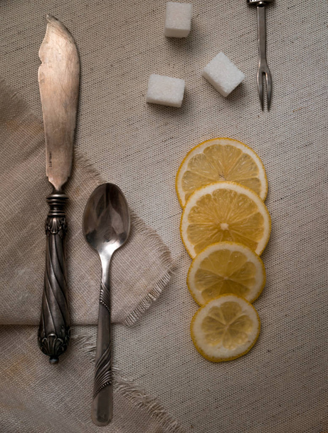 vintage silver cutlery, lemon and refined on canvas, top view - Фото, изображение