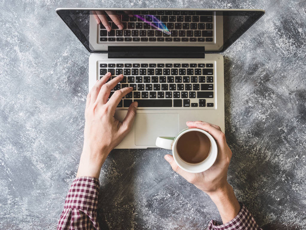 Vue du dessus des mains masculines travaillant sur ordinateur portable et tenant une tasse de café avec fond gris grunge
 - Photo, image