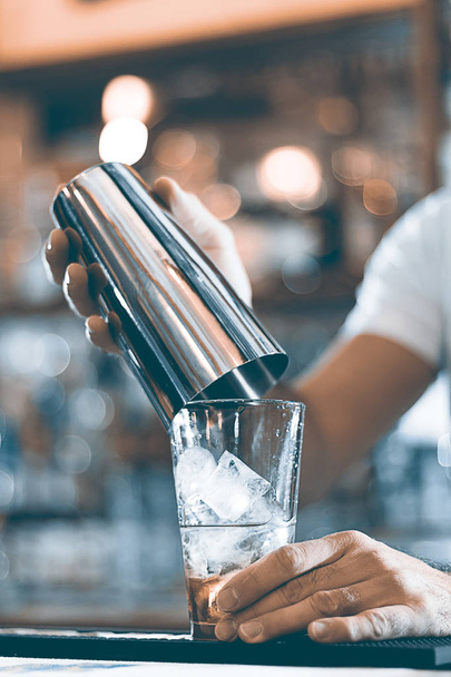 Expert barman is making cocktail at night club cocktail shaker. - Фото, зображення