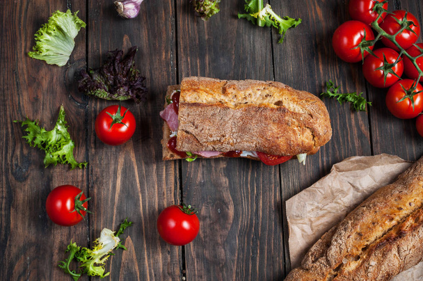 Ciabatta sandwich with prosciutto, cherry tomatoes and salad on dark background - Photo, Image