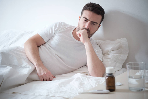 Man feeling bad lying in the bed and looking the thermometer - Photo, Image