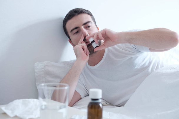 Man feeling cold and using a nasal spray lying in the bed - Fotoğraf, Görsel