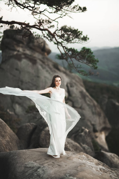 Gorgeous bride in elegant dress holding bouquet posing near forest - Фото, изображение