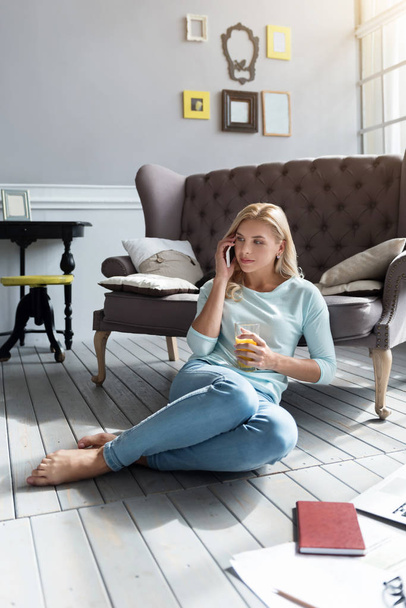 Blond woman sitting on floor and talking per phone - Фото, изображение