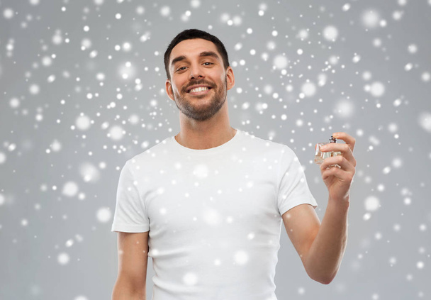 smiling man with male perfume over snow background - Foto, imagen